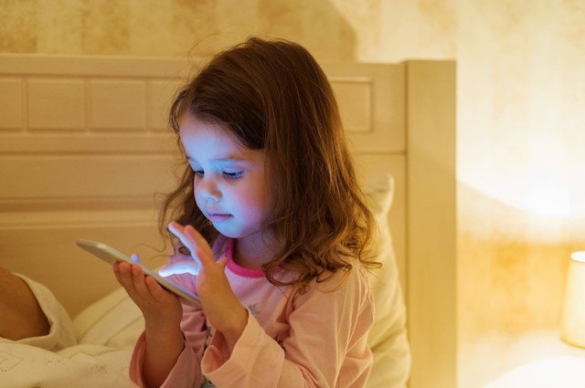 Cute little girl with smartphone lying in a bed, bedtime