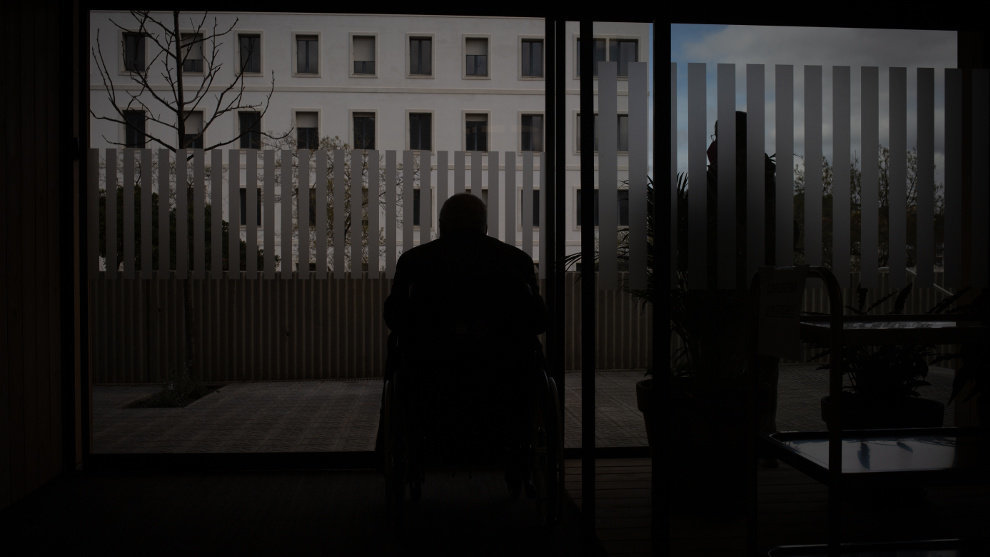 Un hombre en silla de ruedas observa el exterior desde una residencia