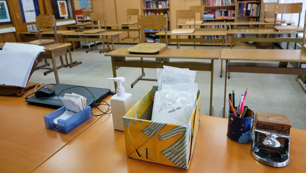 Mascarillas y gel desinfectante en la mesa del profesor de un aula