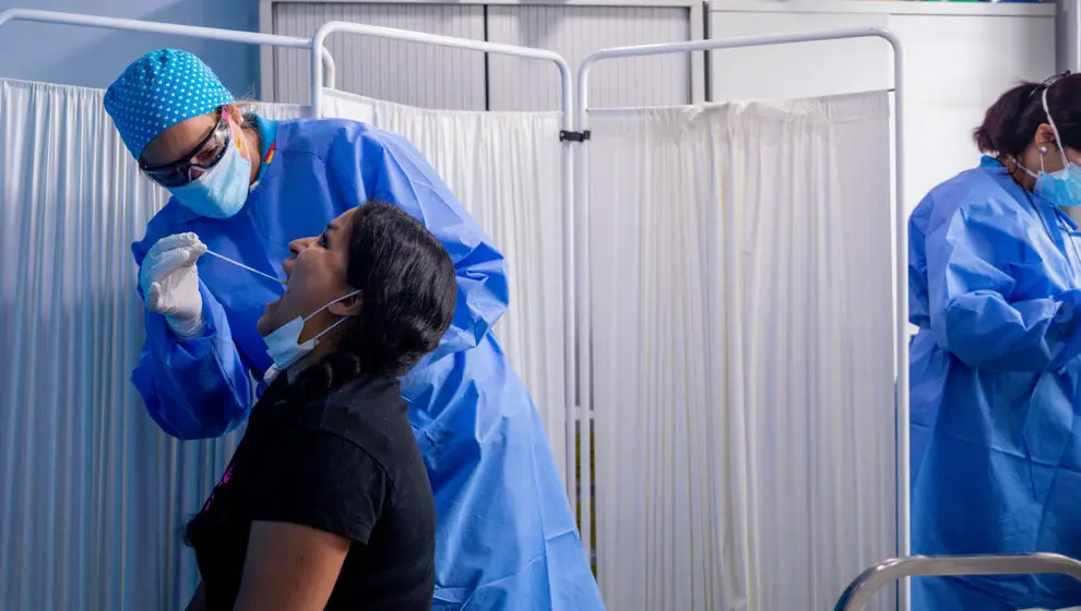 Un trabajador sanitario protegido le realiza a una mujer un test PCR
