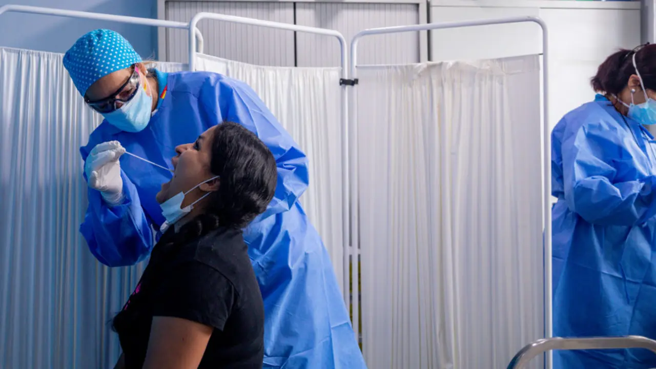 Un trabajador sanitario protegido le realiza a una mujer un test PCR