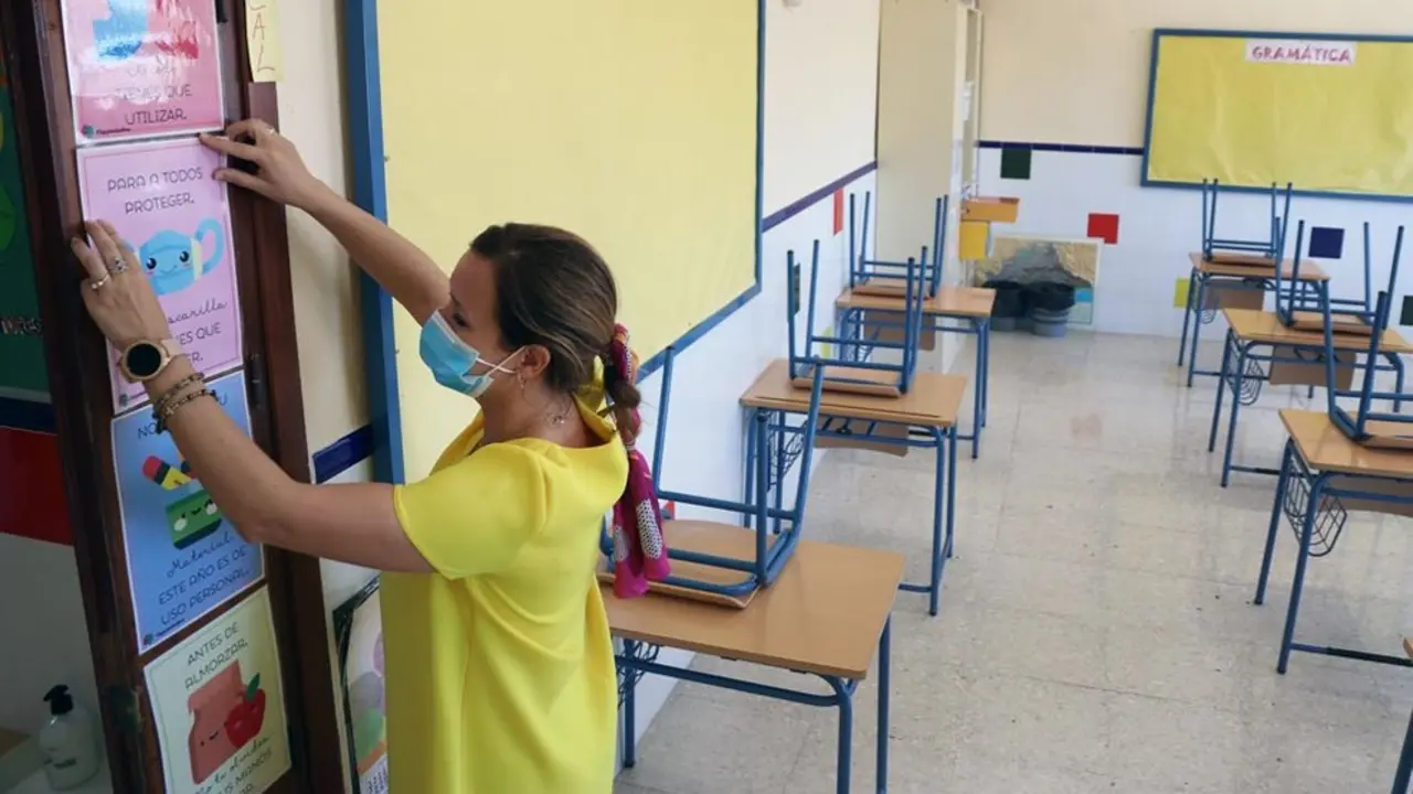Una profesora coloca carteles de medidas preventivas ante el COVID-19 en el aula