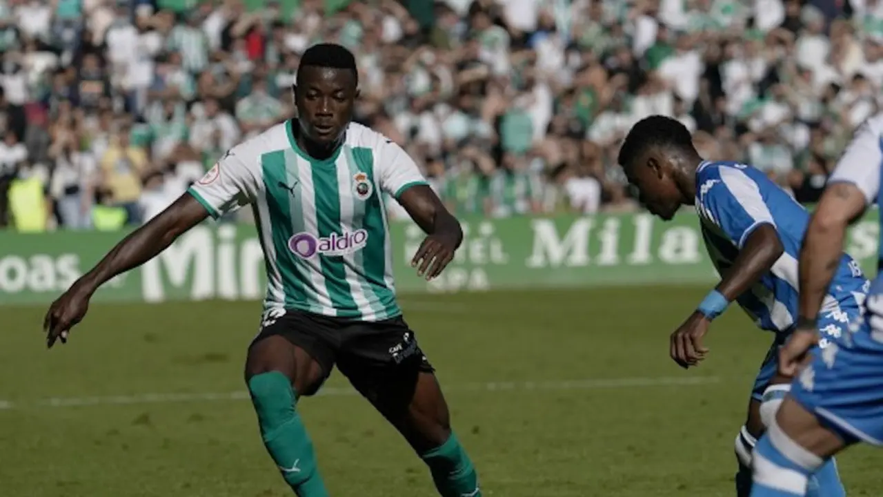 Futbolista del Racing conduce el balón ante la presencia de un jugador del Deportivo