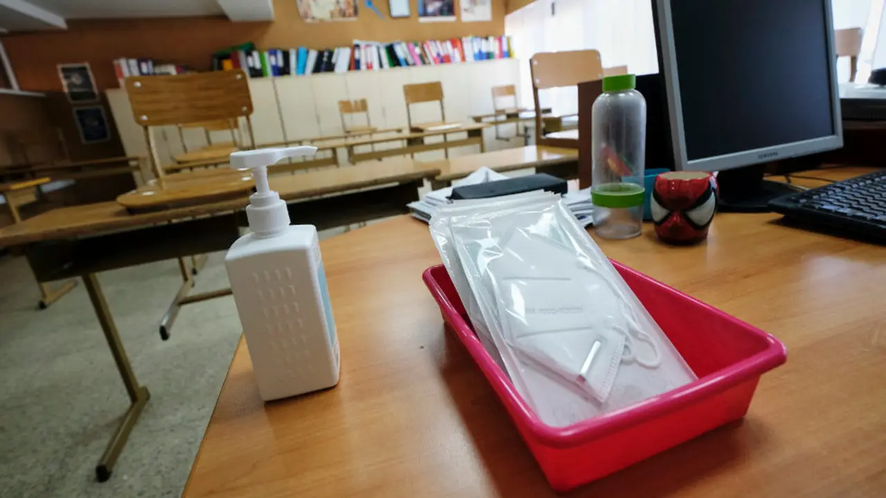 Mascarillas y gel desinfectante en la mesa del profesor de un aula