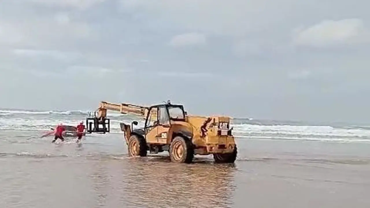 Un veh&iacute;culo pesado saca del mar, en la playa de Oyambre, al turismo que qued&oacute; encallado